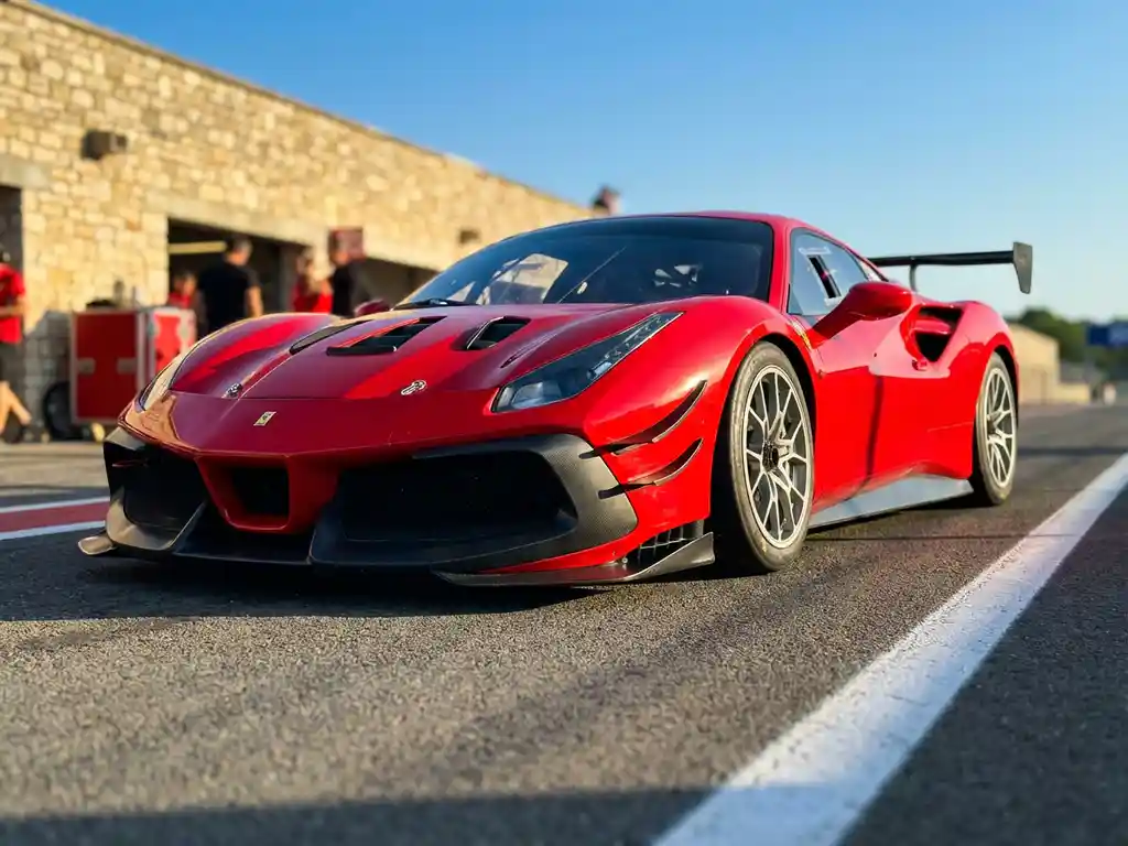 Roter Ferrari 488 Challenge auf sonnenbeschienem Rundkurs, Frontdiffusor und Slicks im Vordergrund, verschwommene Boxenmauer dahinter.