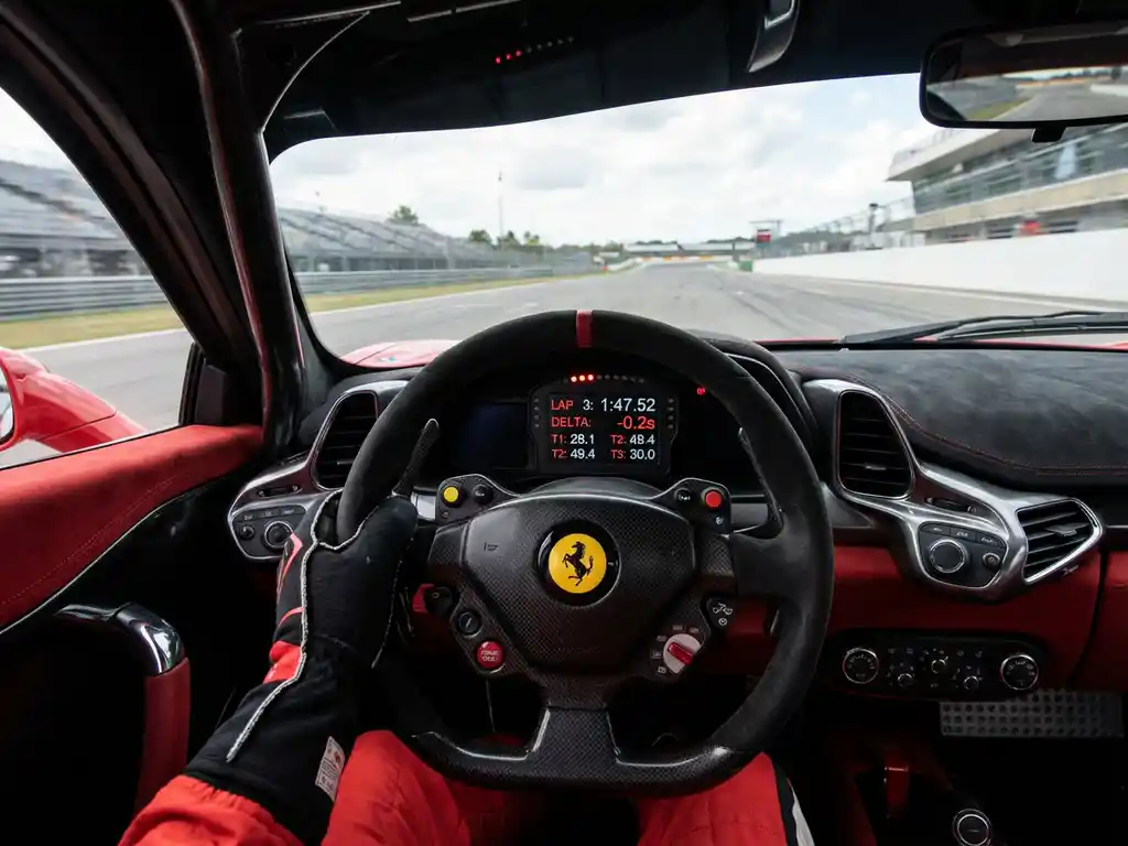 Fahrer im Ferrari Challenge Cockpit mit Alcantara-Lenkrad, digitalem Armaturenbrett und verschwommener Rennstrecke im Hintergrund.