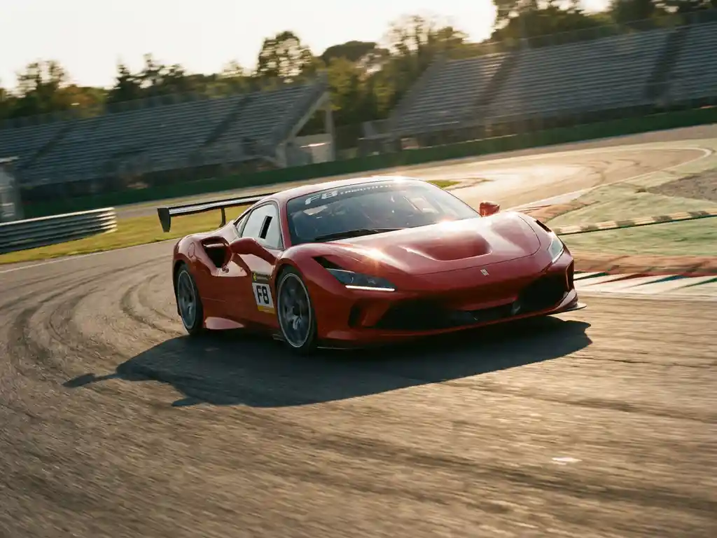 Roter Ferrari-Rennwagen in schneller Kurvenfahrt auf europäischer Rennstrecke, goldenes Nachmittagslicht, Tribünen unscharf im Hintergrund.