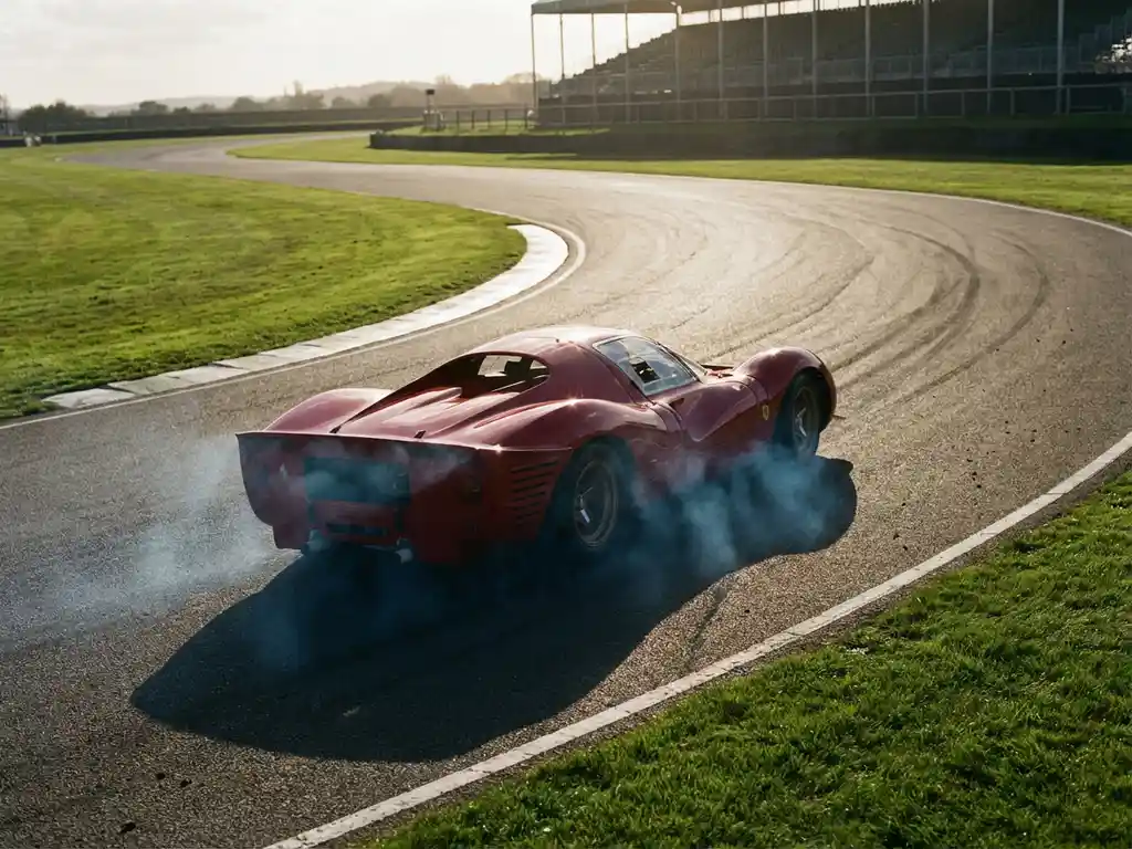 Ferrari-Rennwagen nimmt eine schnelle Kurve mit Reifenrauch am Scheitelpunkt, goldenes Nachmittagslicht, Tribüne im Hintergrund.