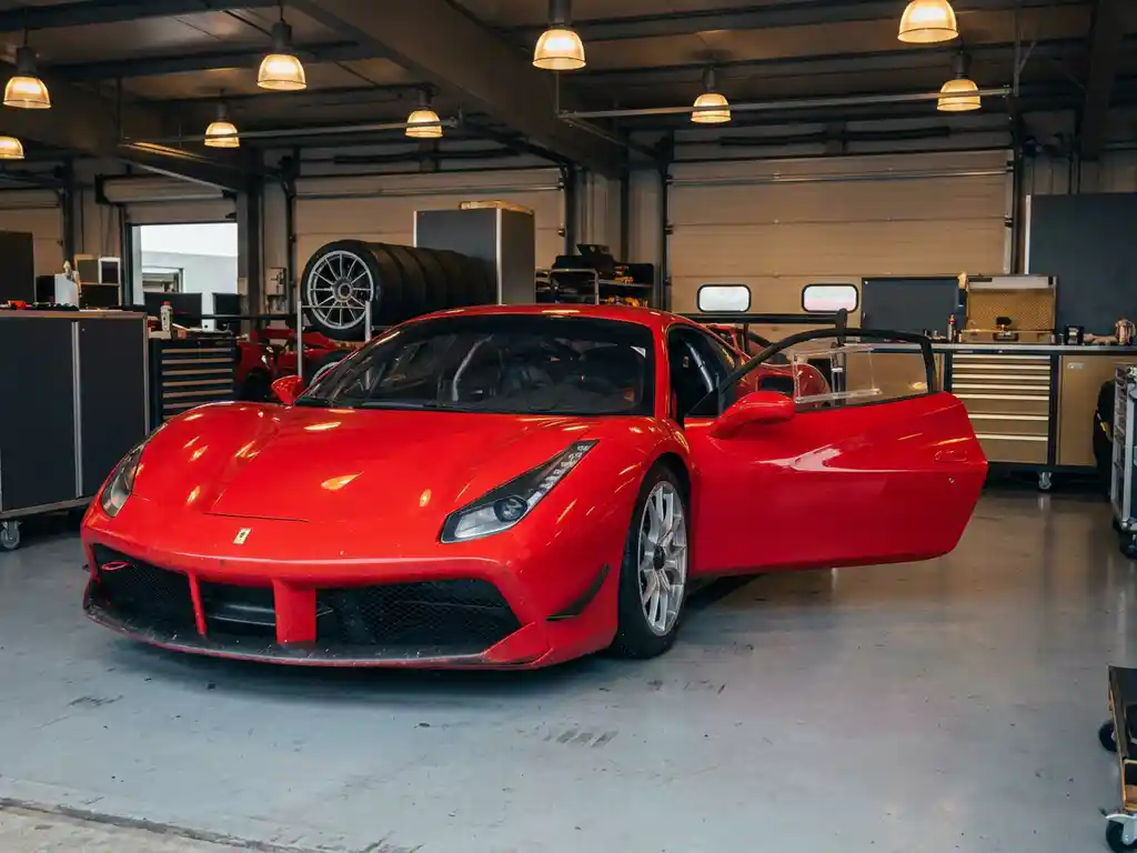 Roter Ferrari Challenge Rennauto in einer Paddock-Garage mit sichtbarem Überrollkäfig, Slick-Reifen und Spuren vergangener Rennen.