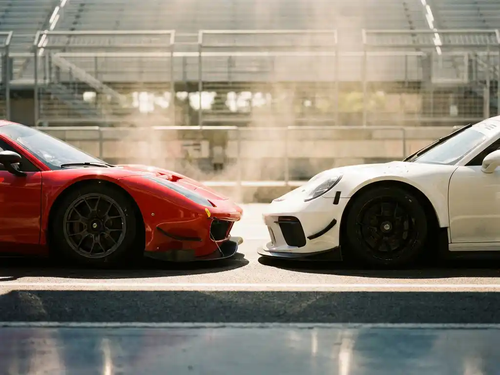 Roter Ferrari und weißer Porsche Rennwagen stehen sich auf sonnenbeschienener Boxengasse gegenüber, Slicks und Aerodynamik im Detail.