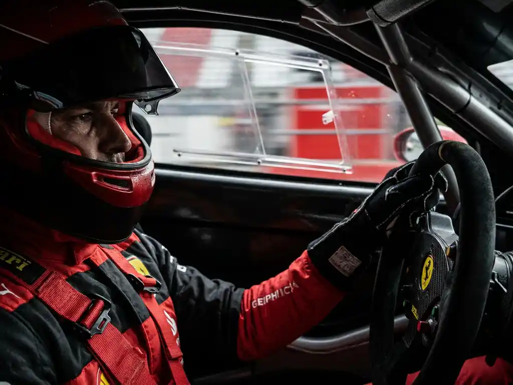 Ferrari-Rennfahrer im Cockpit mit gesenktem Helmvisier, intensivem Blick und verschwommener Boxengasse im Hintergrund.