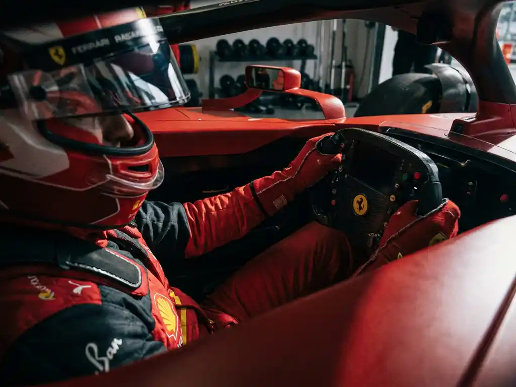 Ferrari-Rennfahrer in rotem Overall und Helm am Steuer eines Cockpits, angespannte Unterarmmuskeln, dramatisches Boxengassenlicht.