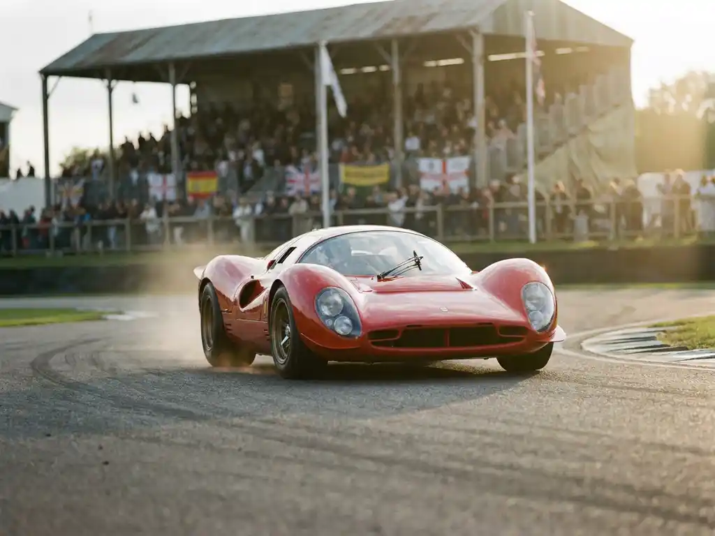 Roter Ferrari-Rennwagen in schneller Kurvenfahrt auf sonnenbeschienem Rundkurs mit verschwommener Tribüne im Hintergrund.