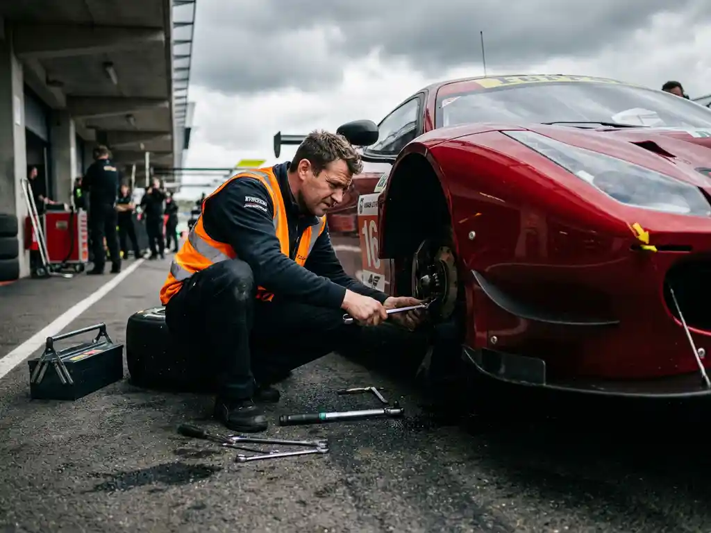 Mechaniker inspiziert die Radaufhängung eines roten Ferrari-Rennautos in der Boxengasse, Werkzeug auf dem Asphalt verstreut.